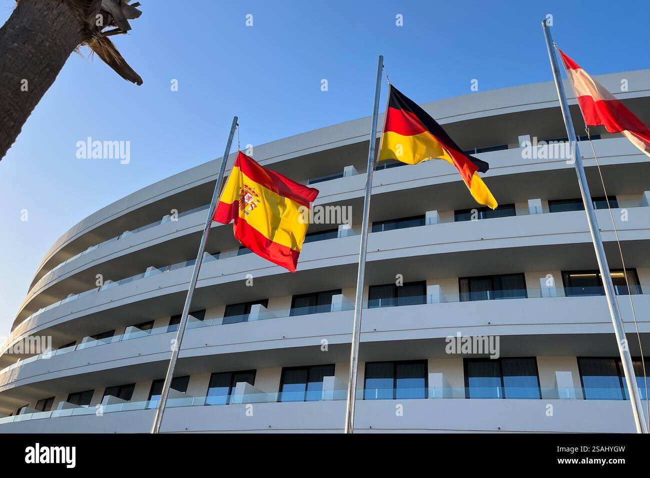 The flags of Spain, Germany, and Austria fluttering in the wind outside the refurbished Mediterranean Palace Hotel, part of the Mare Nostrum Resort. - Smartphone Captured Stock Image