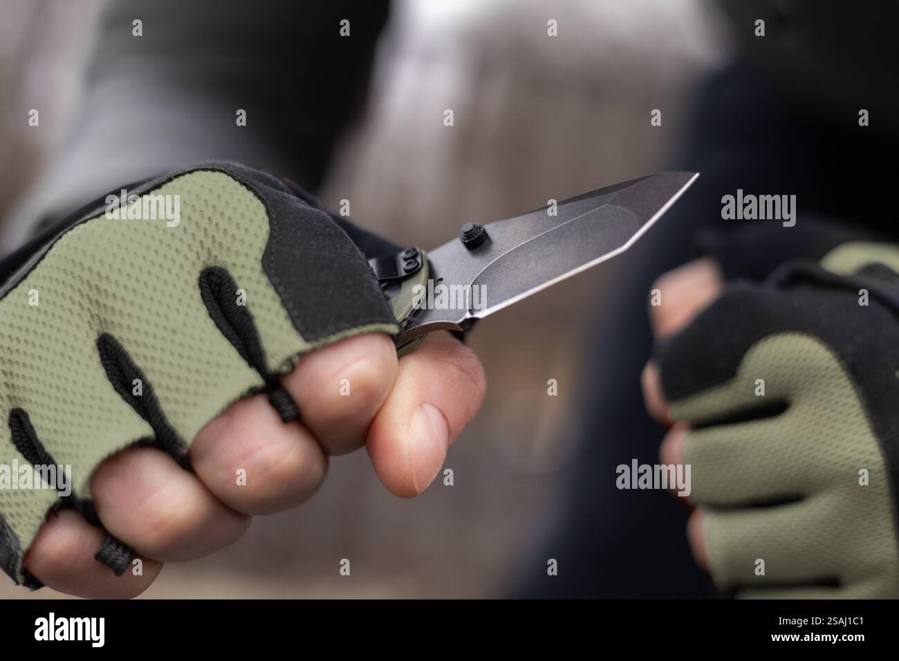 The man wearing tactical gloves using folding knife. Stock Photo