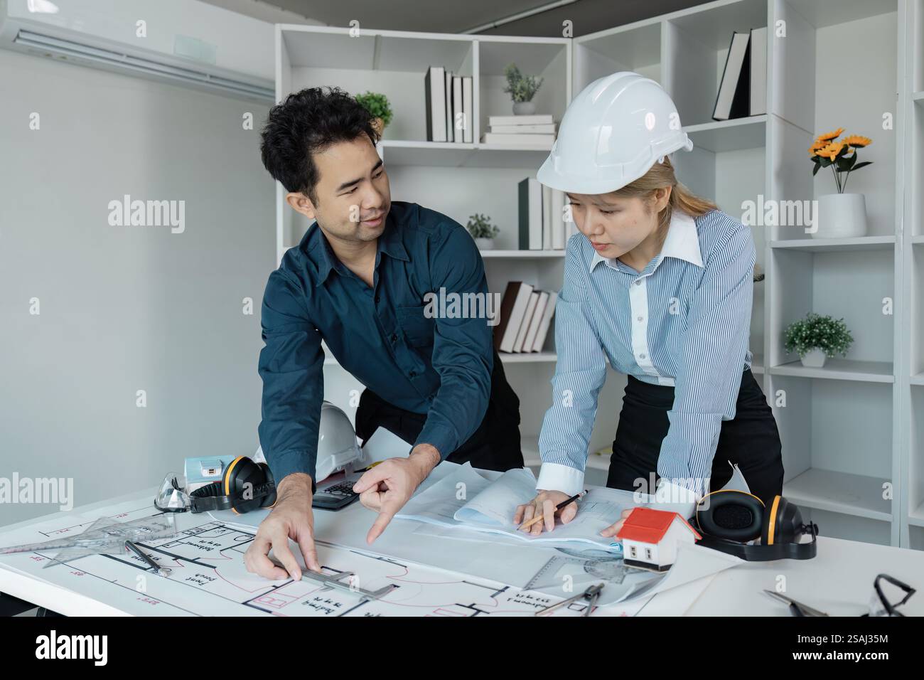 Diverse engineers collaborating on architectural blueprints in an office setting. Stock Photo