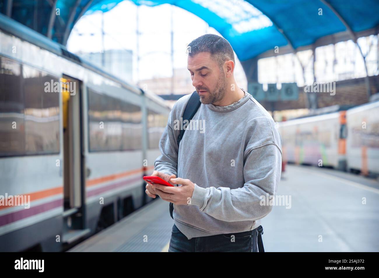 Man Using Smartphone While Waiting at Train Station Stock Photo