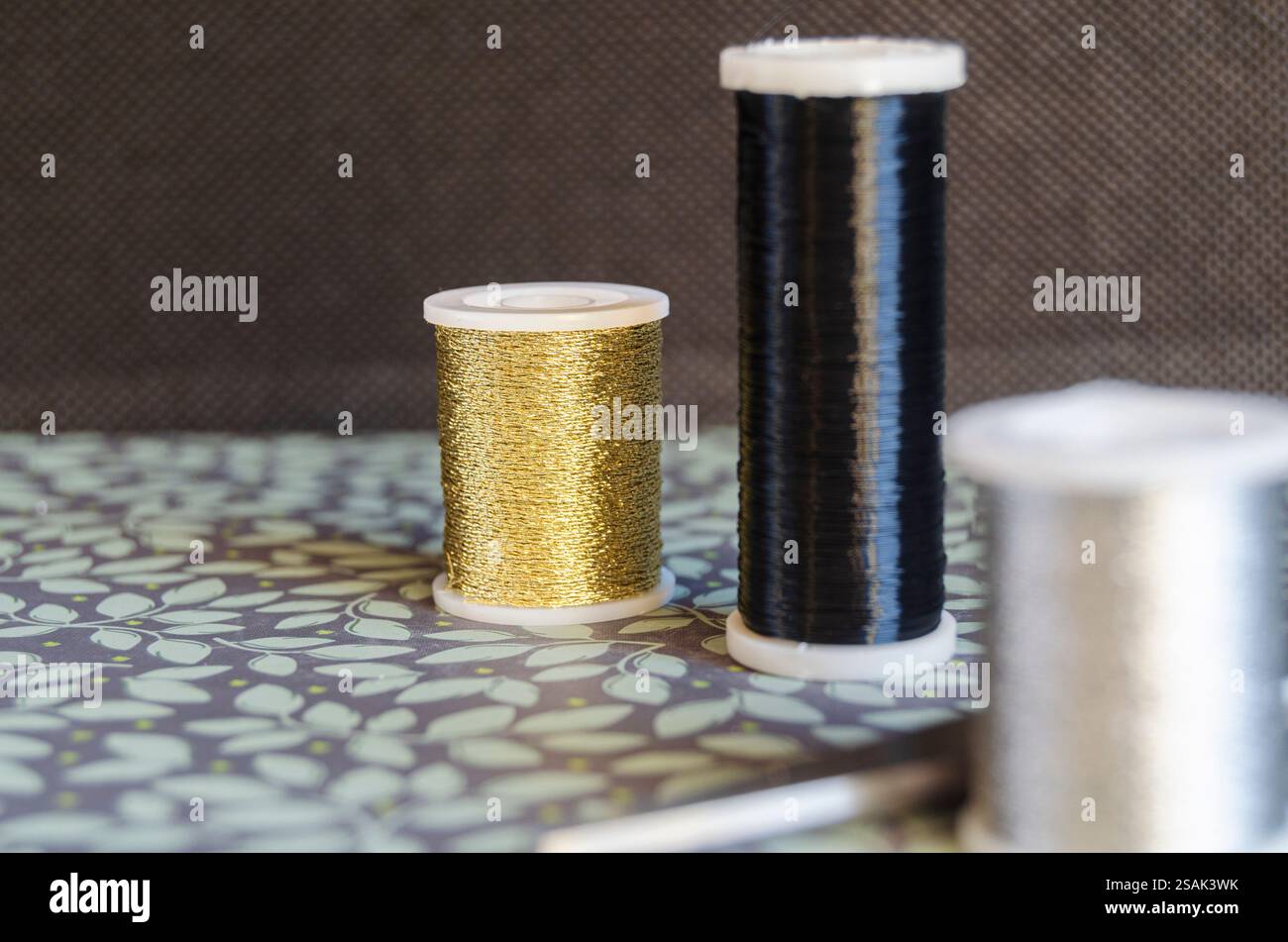Reels of metalic thread, gold, silver and black on a green floral ...