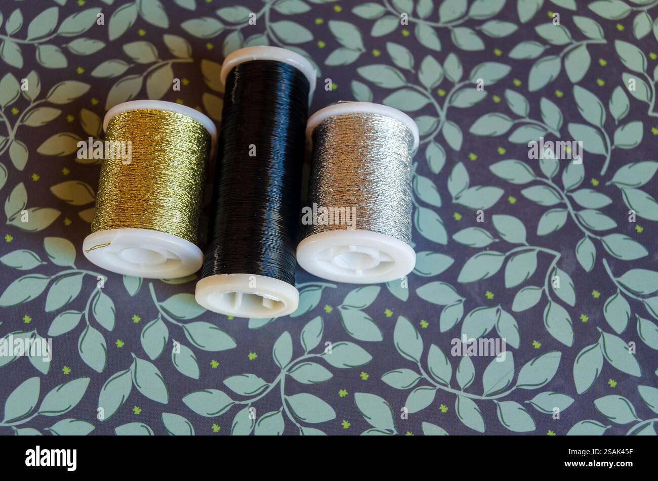 Reels of metallic thread, gold, silver and black on a green floral ...