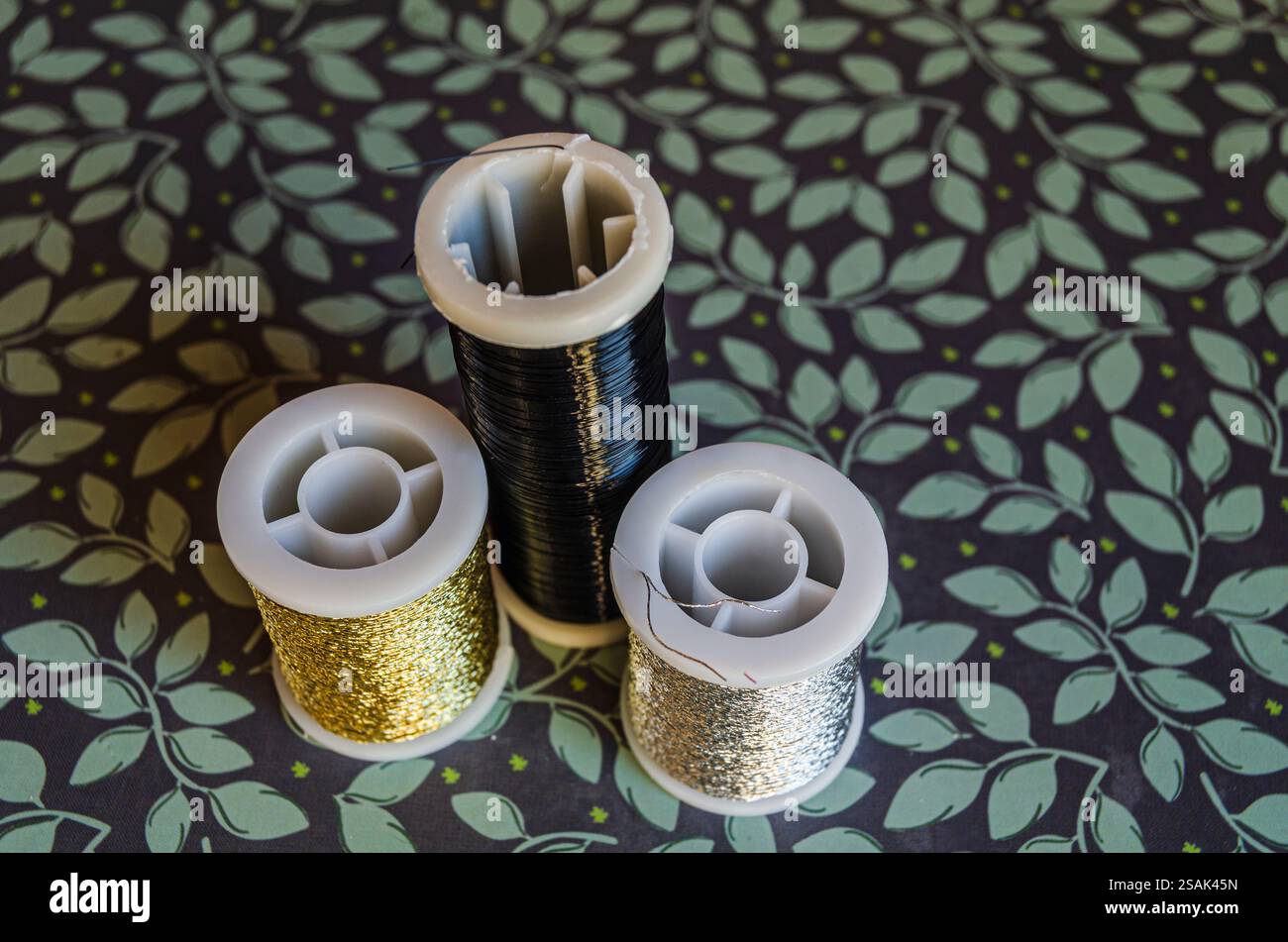 Reels of metallic thread, gold, silver and black on a green floral ...