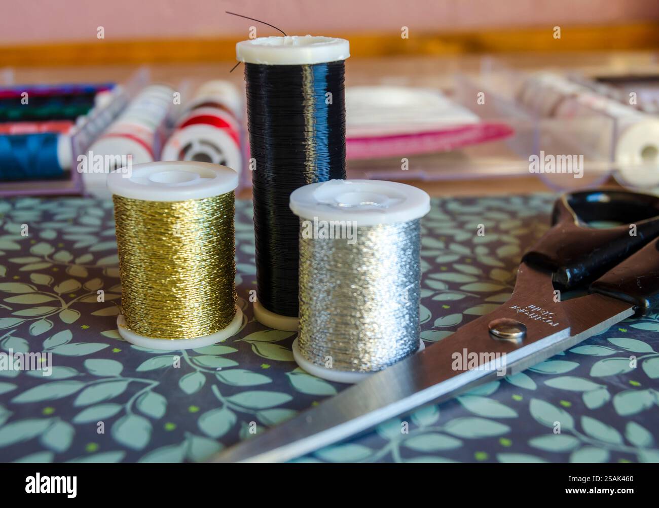 Reels of metalic thread, gold, silver and black on a green floral ...