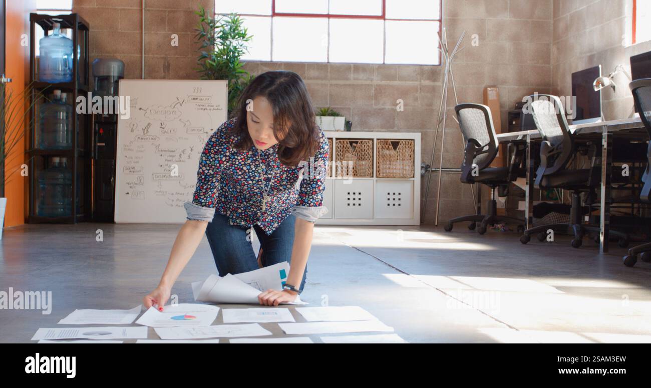 Female Designer Planning Campaign Laying Out Documents On Floor Of Modern Office Stock Photo