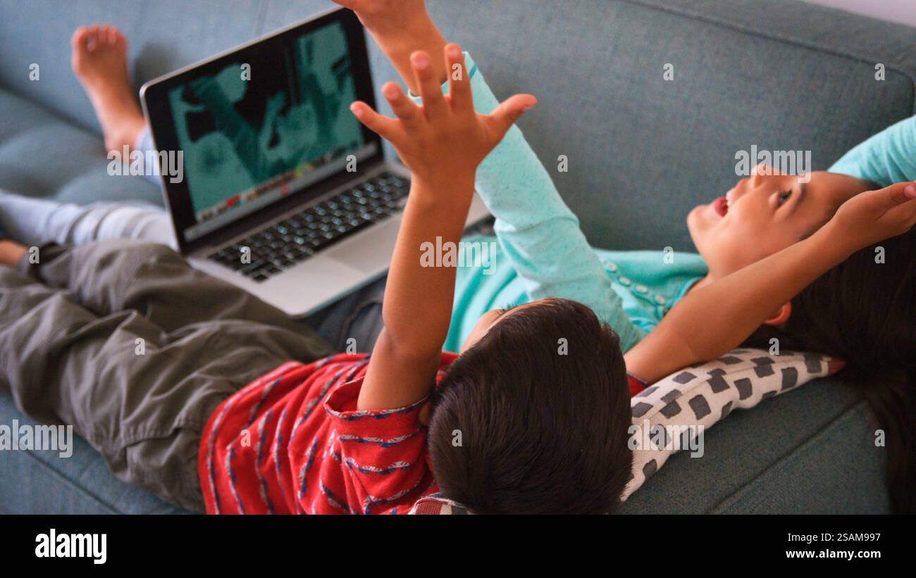 Over The Shoulder Shot Brother And Sister Sitting On Sofa At Home Using ...