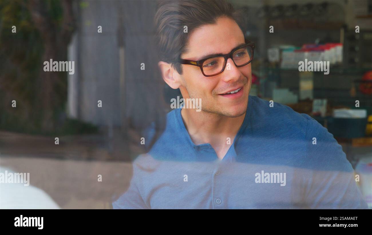 View Through Window Of Smiling Young Man Meeting Friends In Coffee Shop Stock Photo