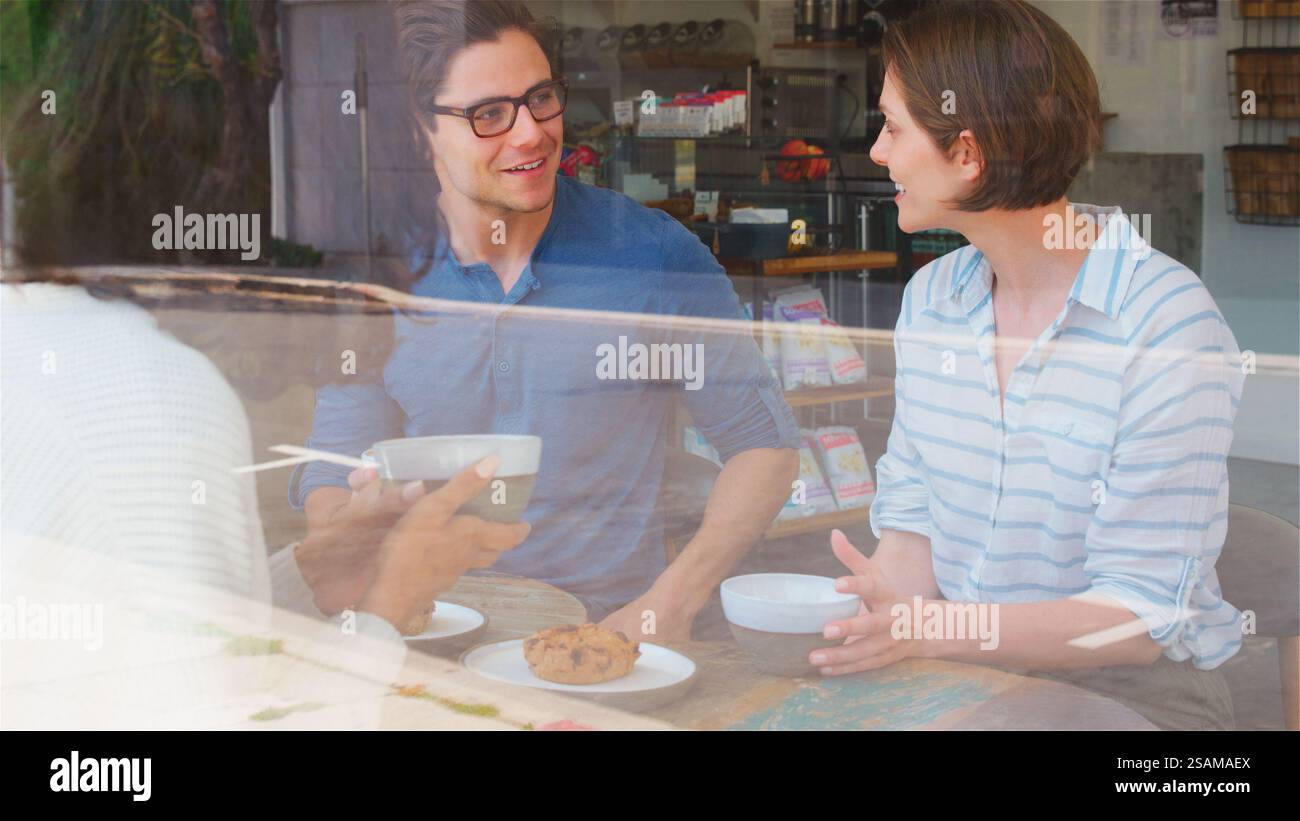 View Through Window Of Smiling Young Man Meeting Friends In Coffee Shop Stock Photo
