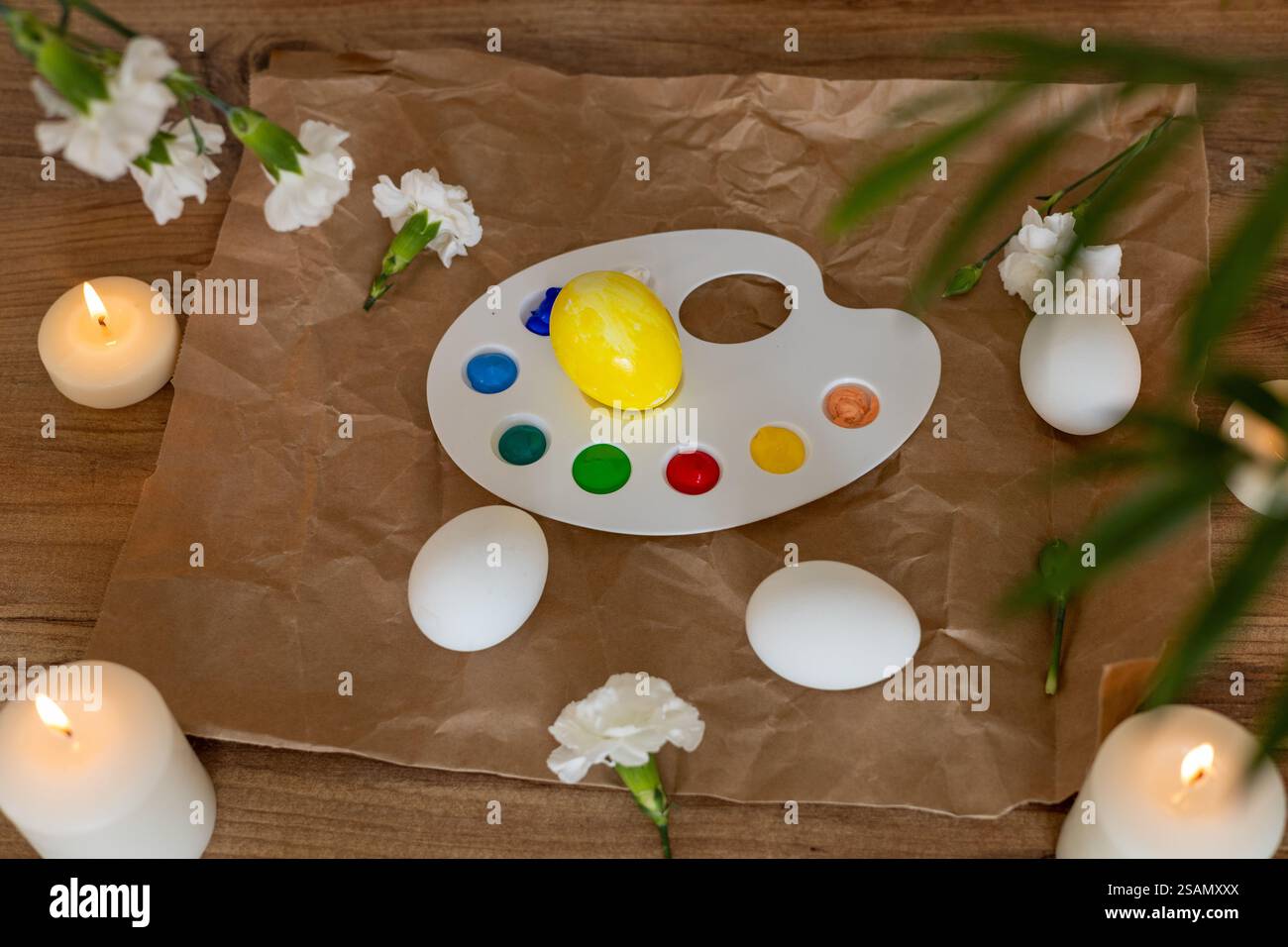 Creative Easter egg decorating activity with candles and flowers in spring setting Stock Photo