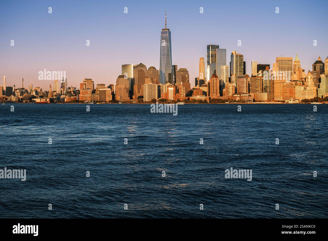 The New York City skyline at golden hour and is viewed from across the Hudson River. Freedom Tower stands tall among modern skyscrapers, reflecting. Stock Photo