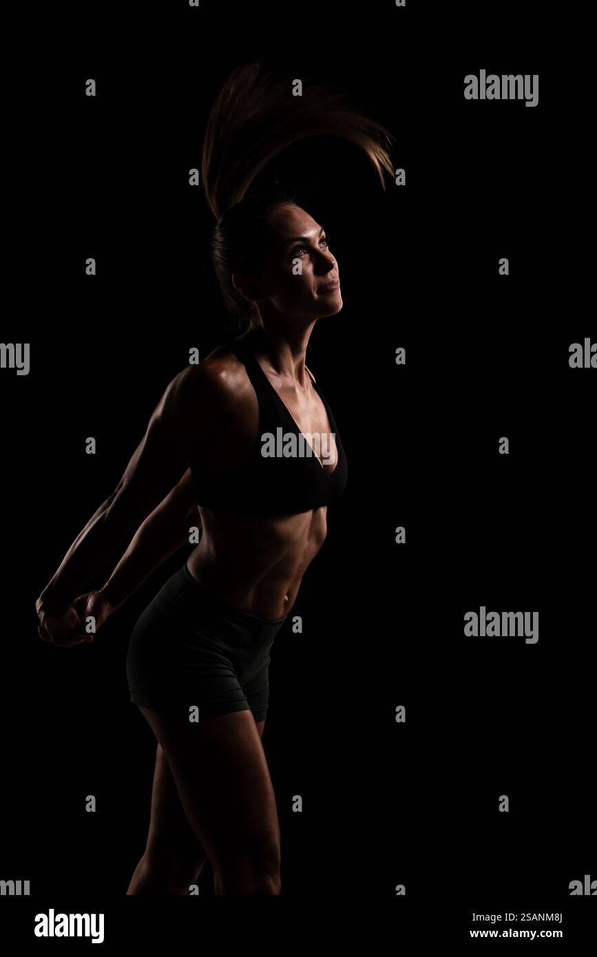 Female fitness model showcasing strength and posture under dark ...