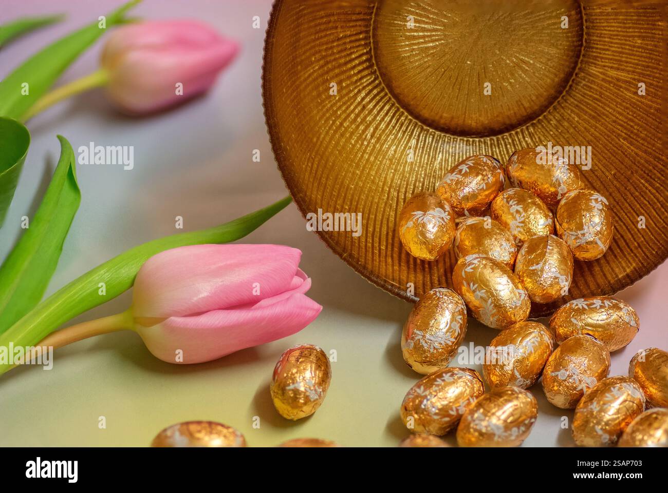Gold foiled Easter eggs and pink tulips, close up; Happy Easter, Easter celebration, Spring celebration. Stock Photo