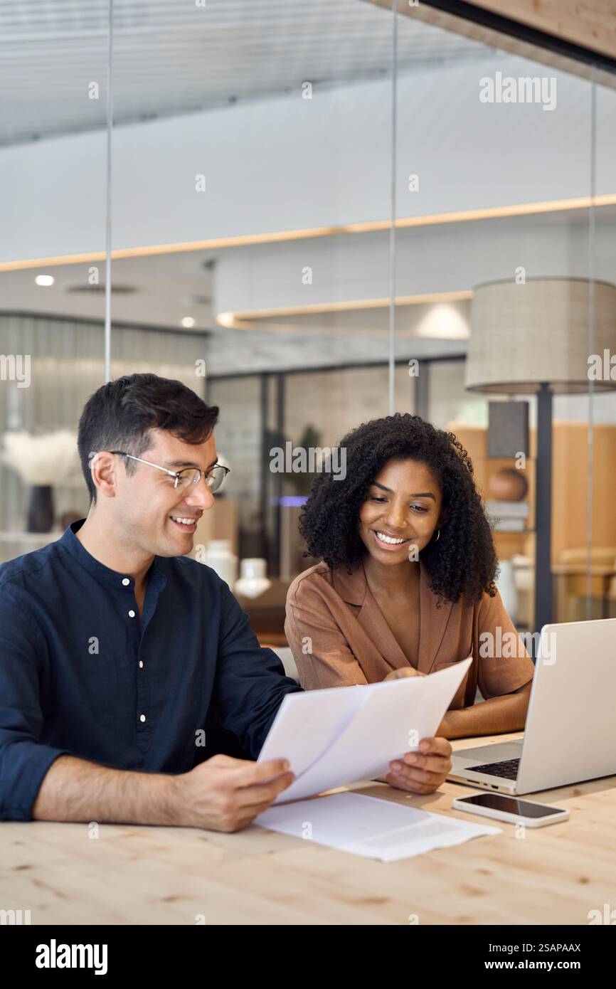 Diverse professional partners using laptop discussing documents in office. Stock Photo