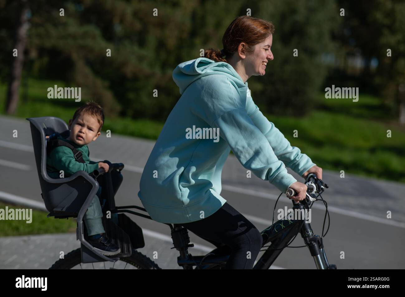 Caucasian woman riding a bicycle with her toddler son sitting behind ...