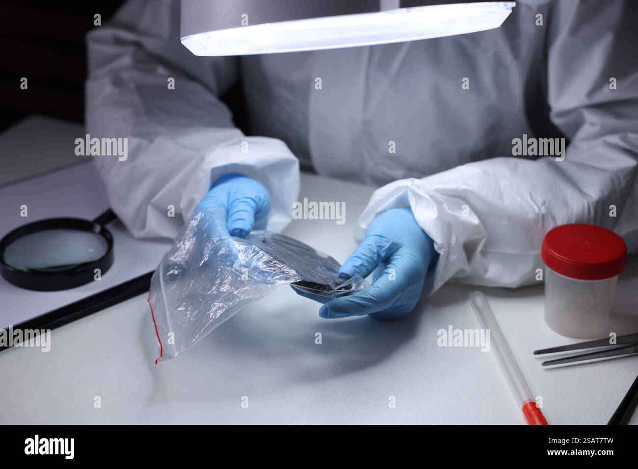 Forensic expert examining evidence in plastic bag at table indoors ...