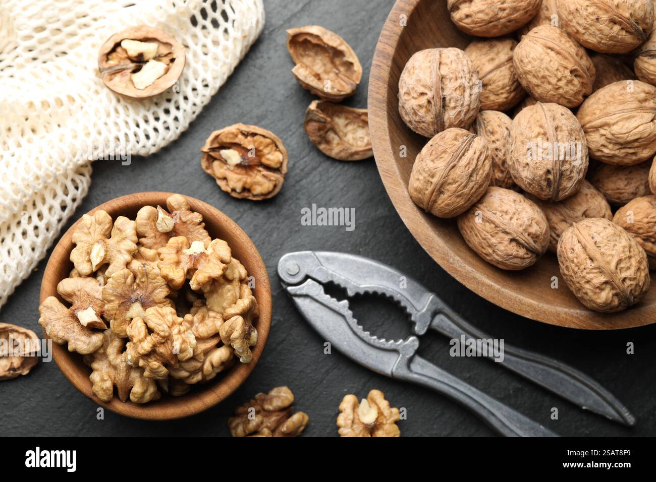 Fresh ripe walnuts, nutcracker and shells on black table, flat lay Stock Photo
