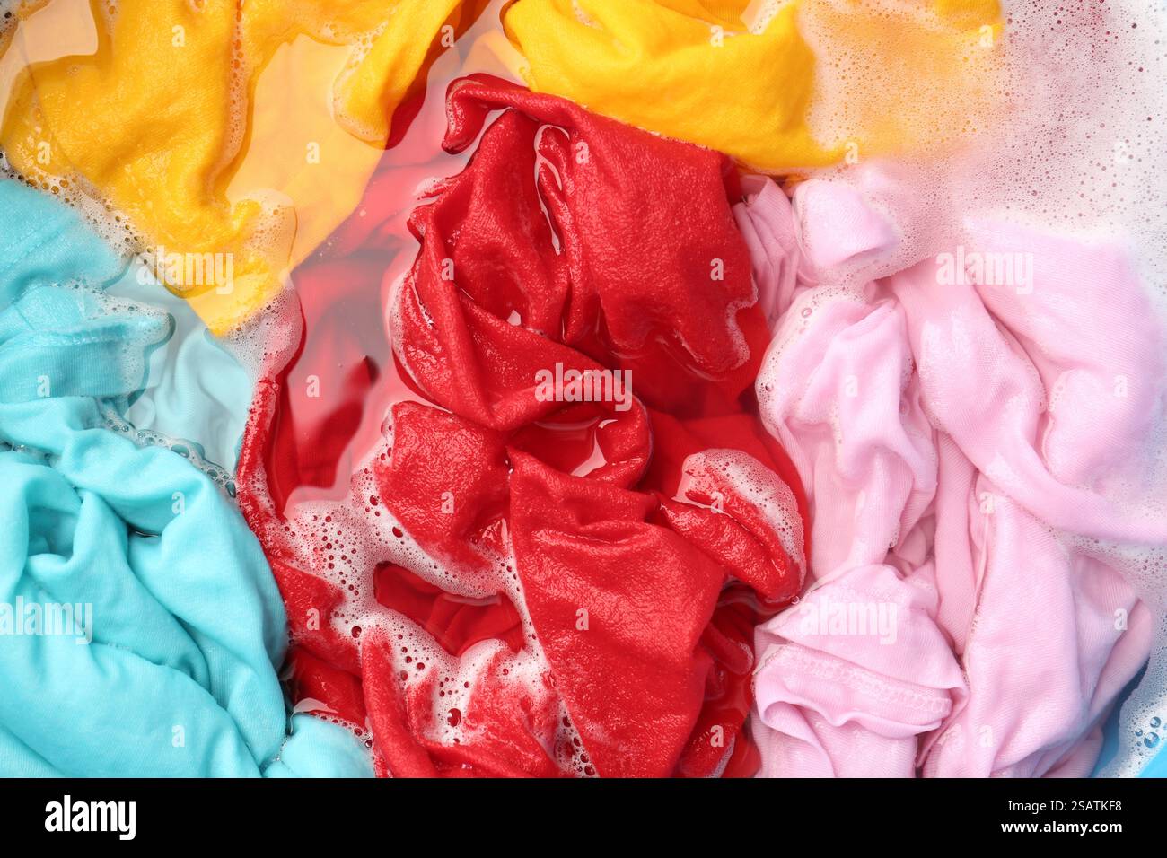 Colorful clothes soaked in water before washing, top view Stock Photo ...