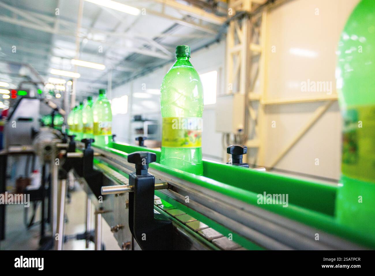 Bottles of green liquid moving along a conveyor belt in a factory ...