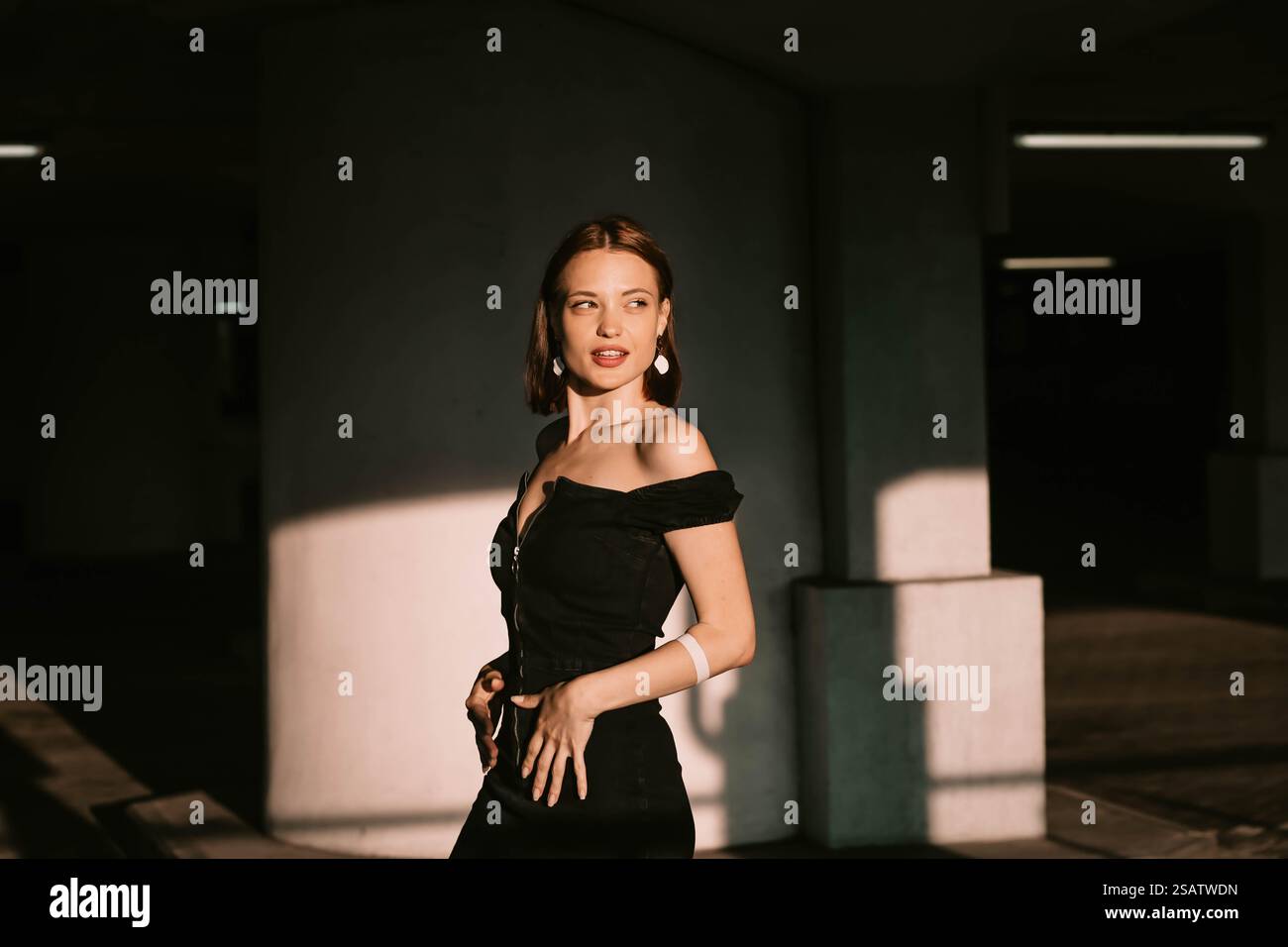 Woman in a black dress poses confidently in soft lighting with shadows and modern style Stock Photo