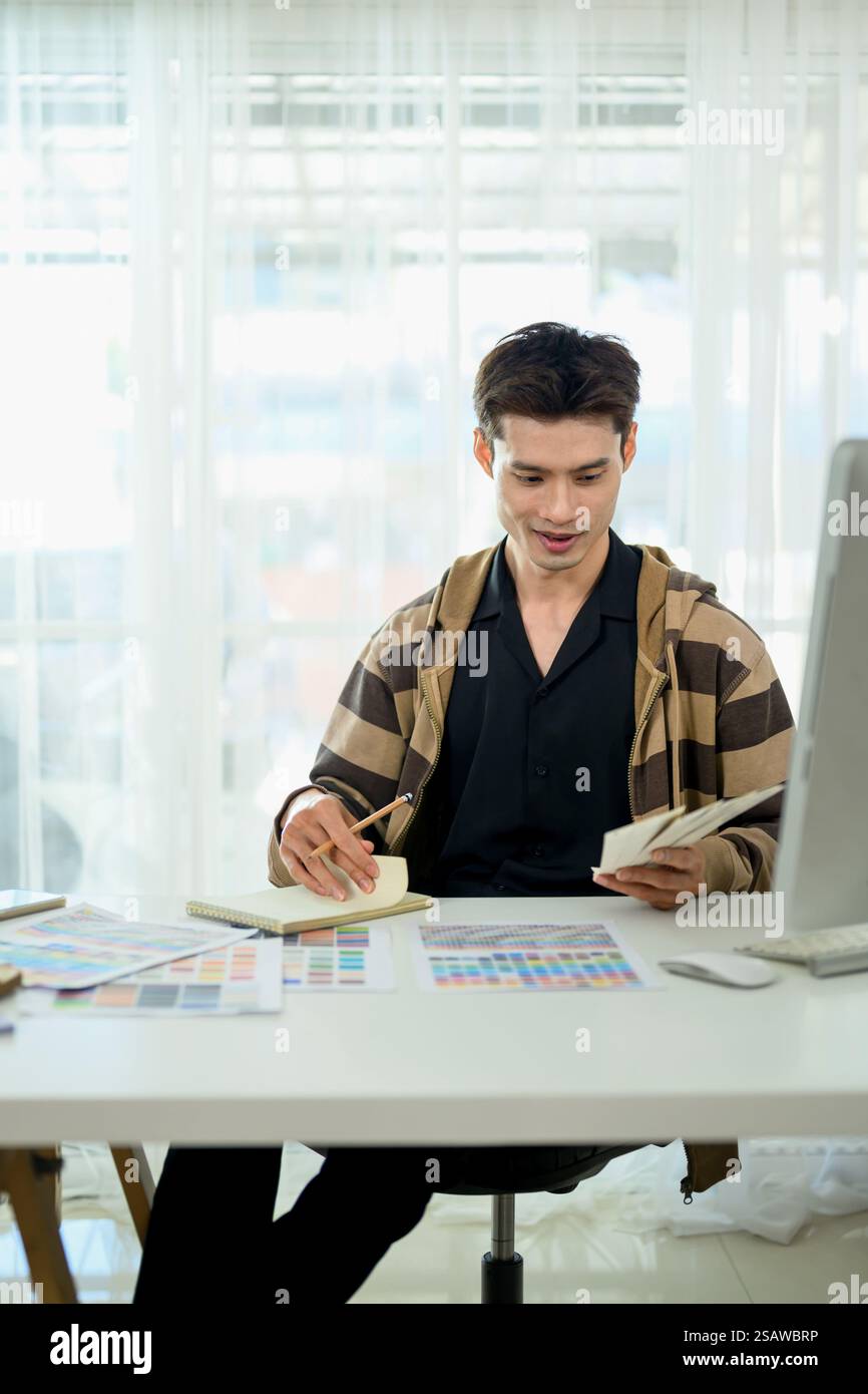 Male designer sitting at modern workspace reviewing color swatches and ...