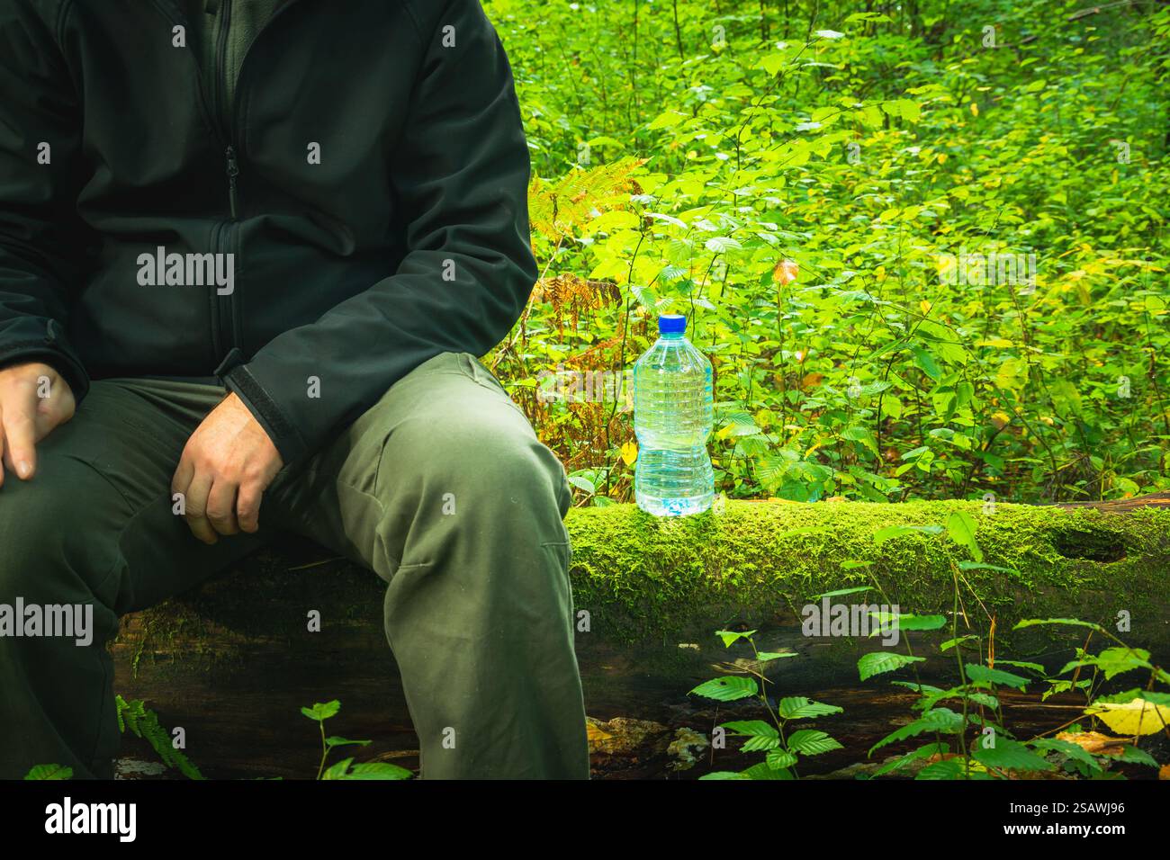 A man sitting on a tree trunk and a plastic bottle of water Stock Photo