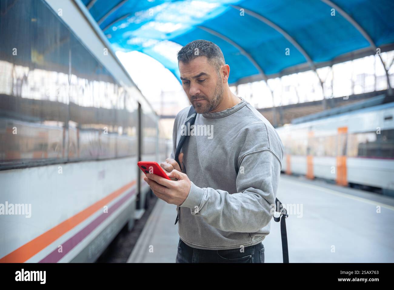 Man Using Red Smartphone at Train Station Stock Photo