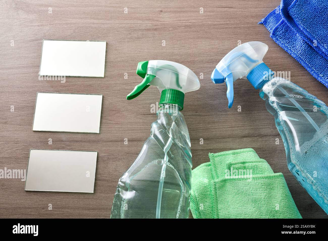 Cleaning products for dirt and dust in a transparent plastic bottle spray on wooden table with microfibre cloths and glass. Top view. Stock Photo