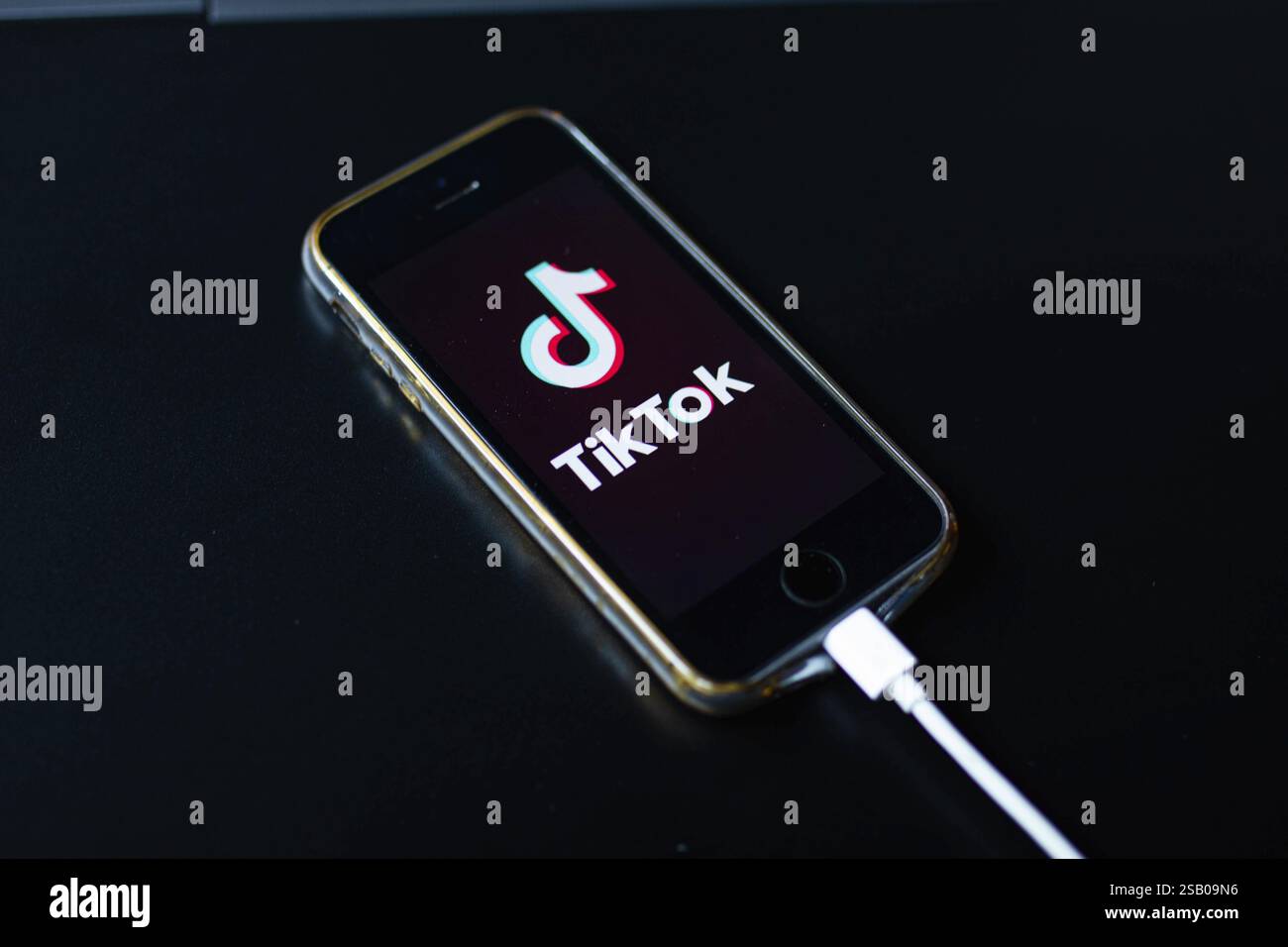 A smartphone placed on a black table showing the TikTok app screen while charging Stock Photo