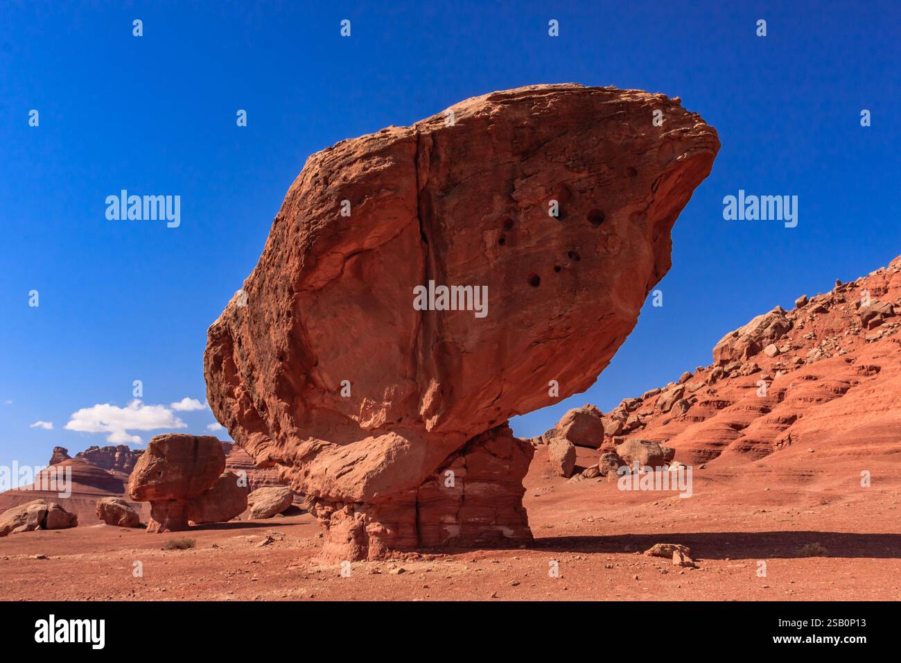 A large rock formation sits in the desert, with a clear blue sky above ...