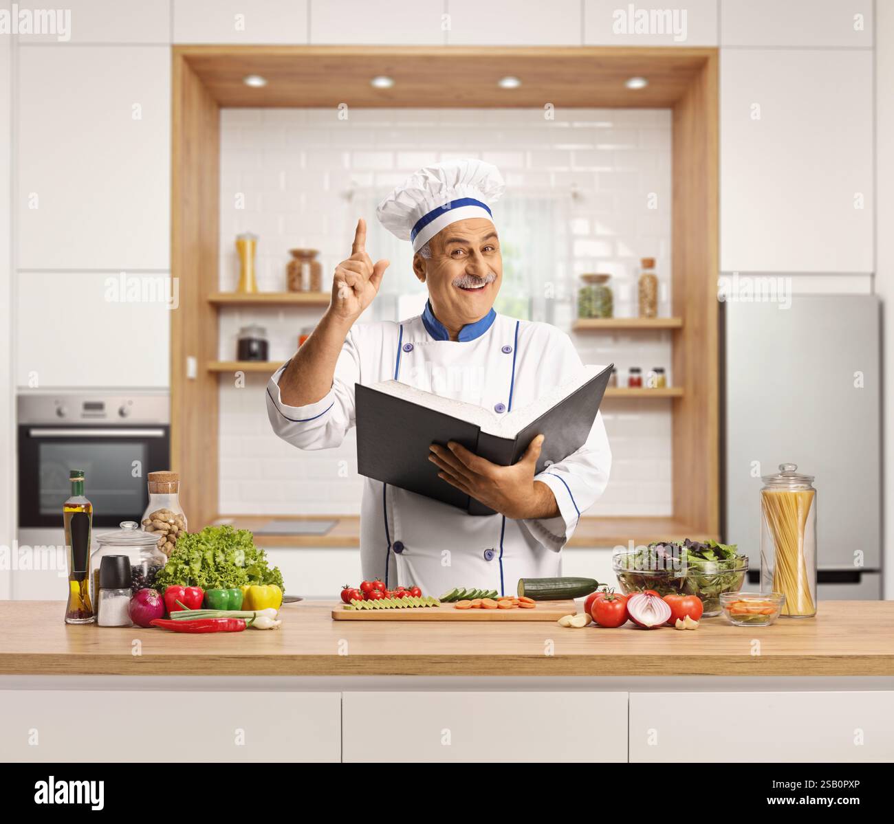 Mature male chef cooking in a kitchen and holding a cook book Stock Photo