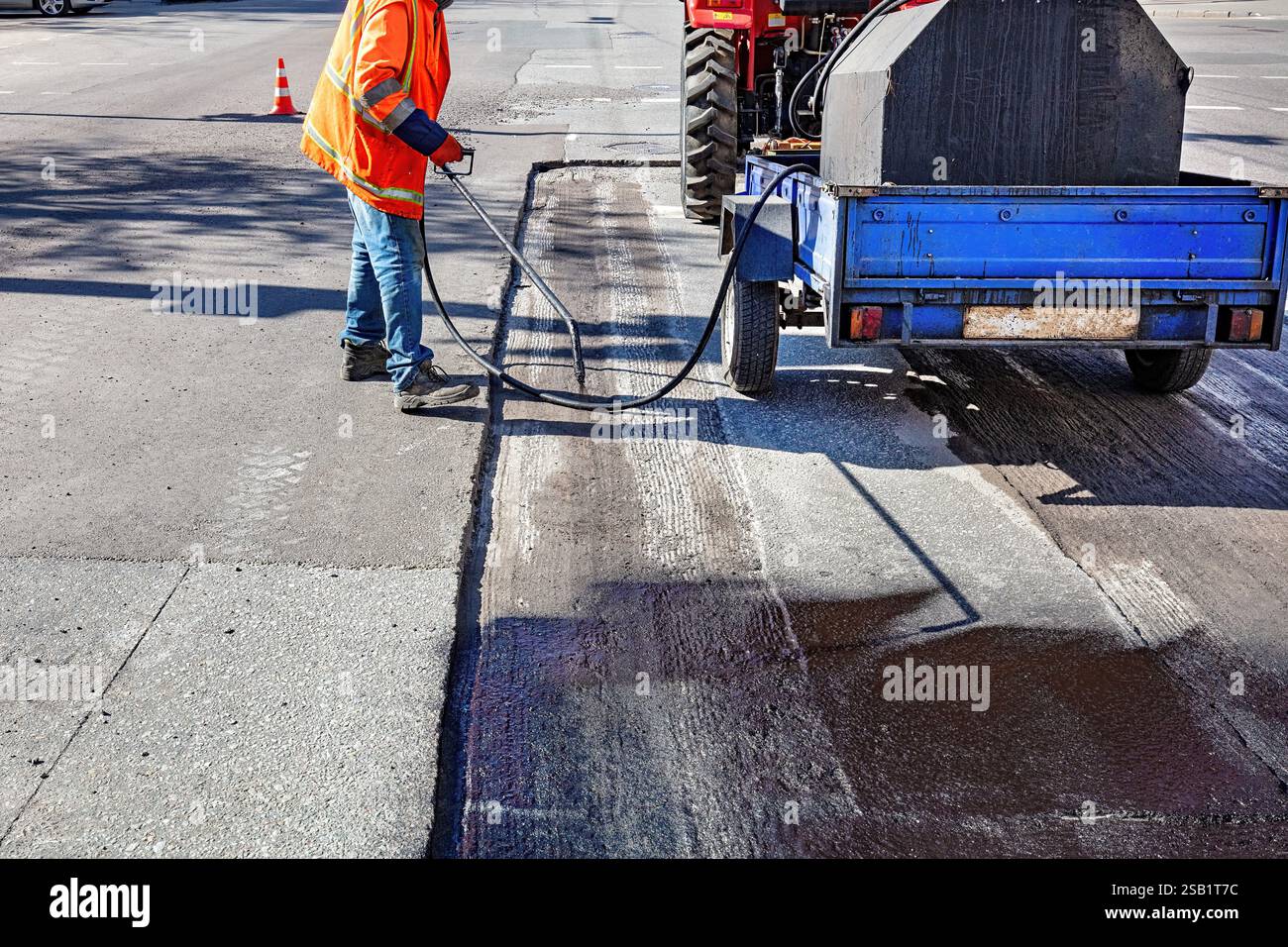 Road worker applying sealant on freshly paved street at mid-morning in an urban area. Stock Photo