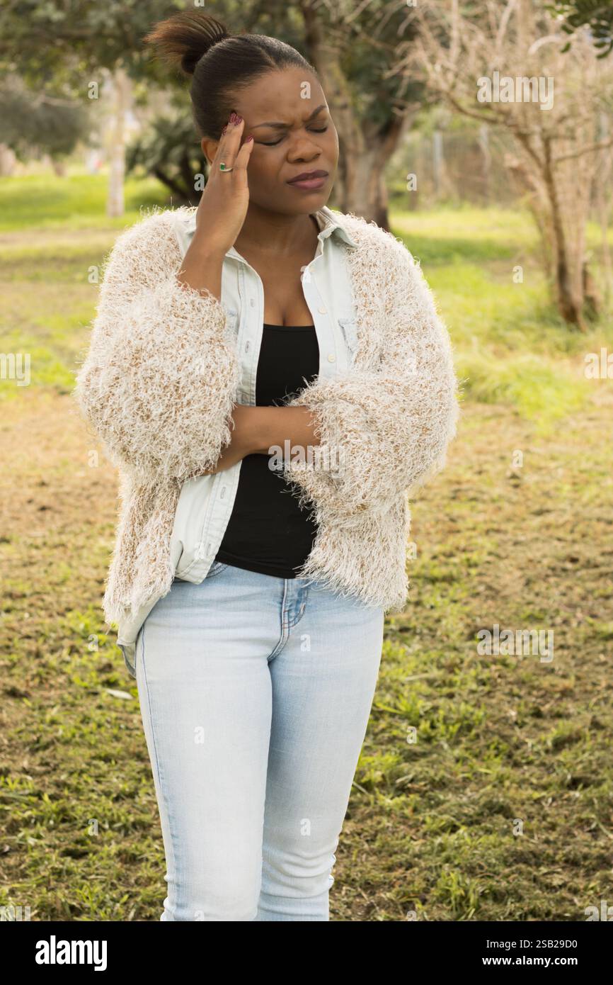 A black woman is standing outdoors with her eyes closed, pressing her ...