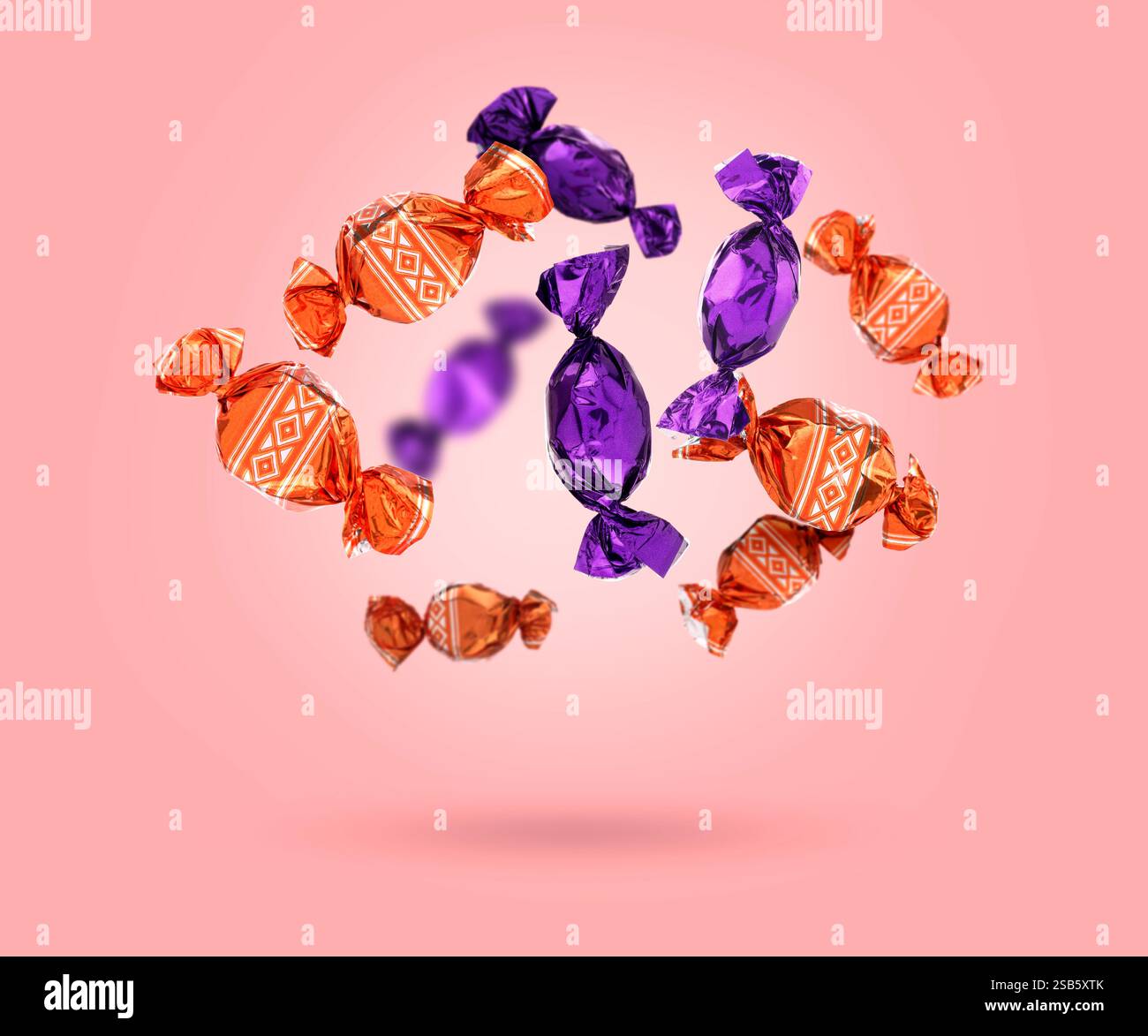 Candies in bright wrappers falling on pink background Stock Photo