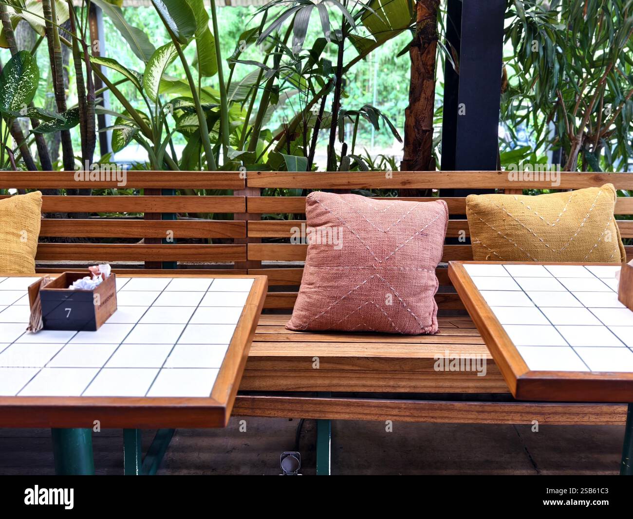 Seminyak, Bali, Indonesia  :An outdoor café seating area featuring a wooden bench, decorative pillows, and tiled tables with a tropical plant ambiance Stock Photo