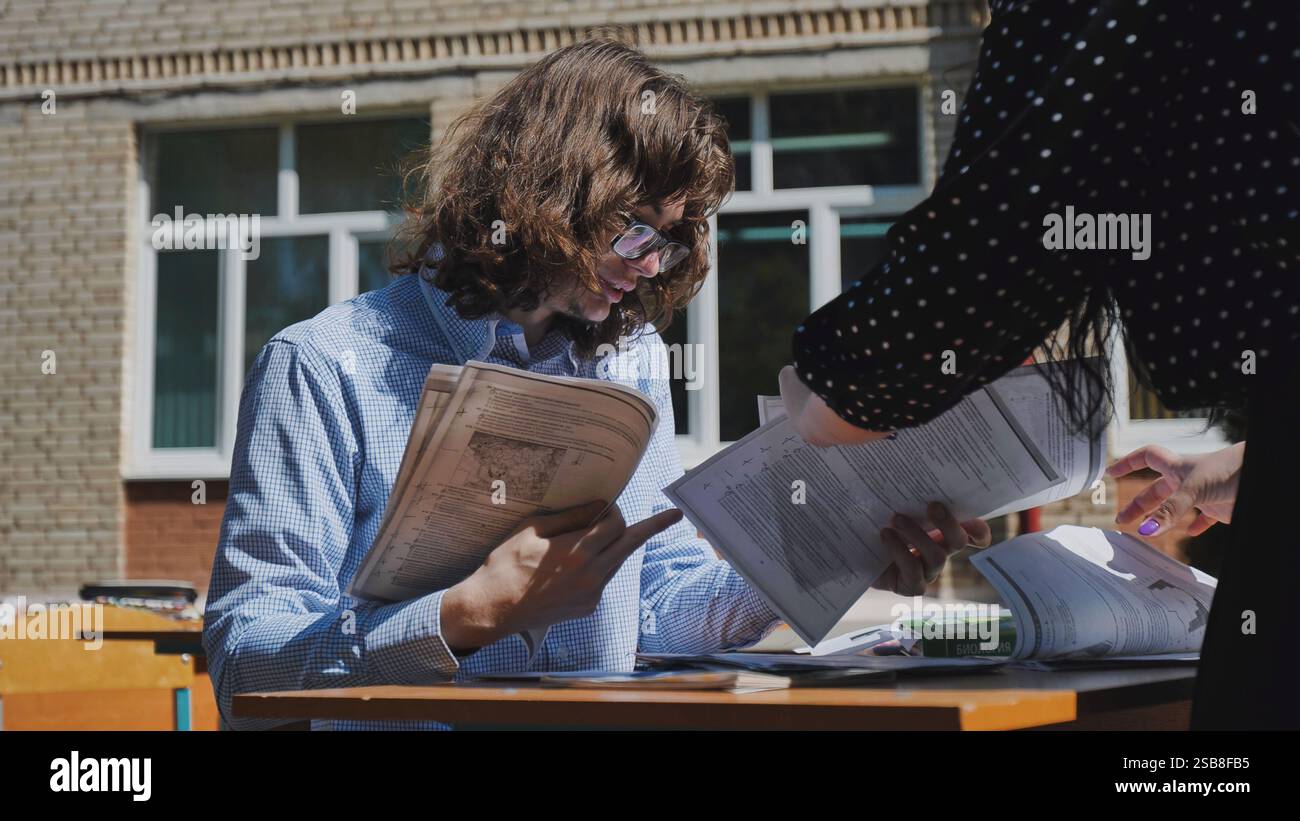 Two high school students collaborate on a project at an outdoor table, exchanging ideas and discussing documents Stock Photo