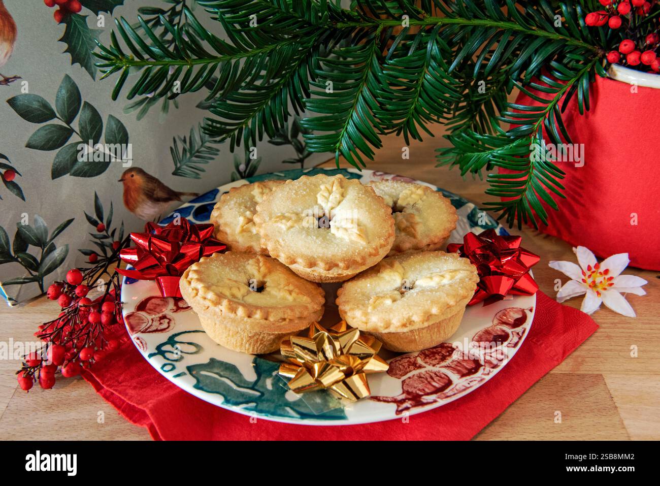 Mince Pies on festive plate with bows and Yew over hanging with berries and Christmas present behind. Stock Photo