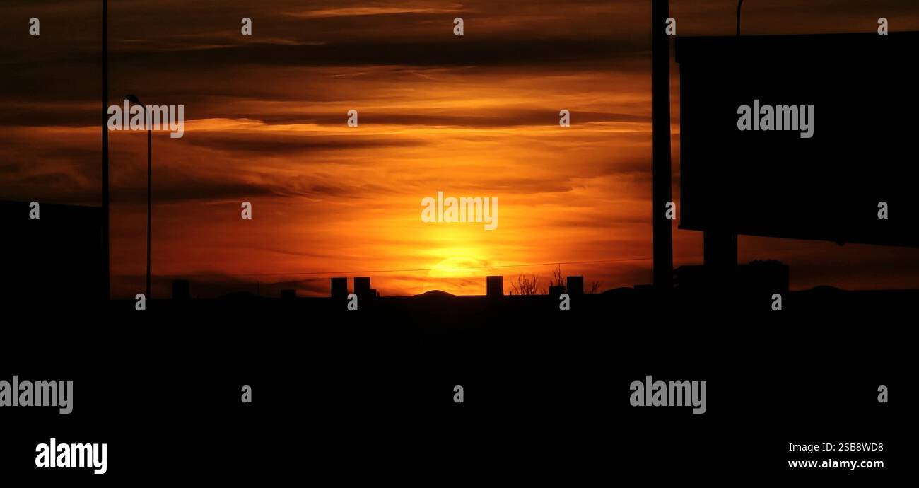 Stunning urban sunset with a vibrant orange sky and silhouetted structures in the foreground, capturing the beauty of cityscapes at dusk. - Smartphone Captured Stock Image