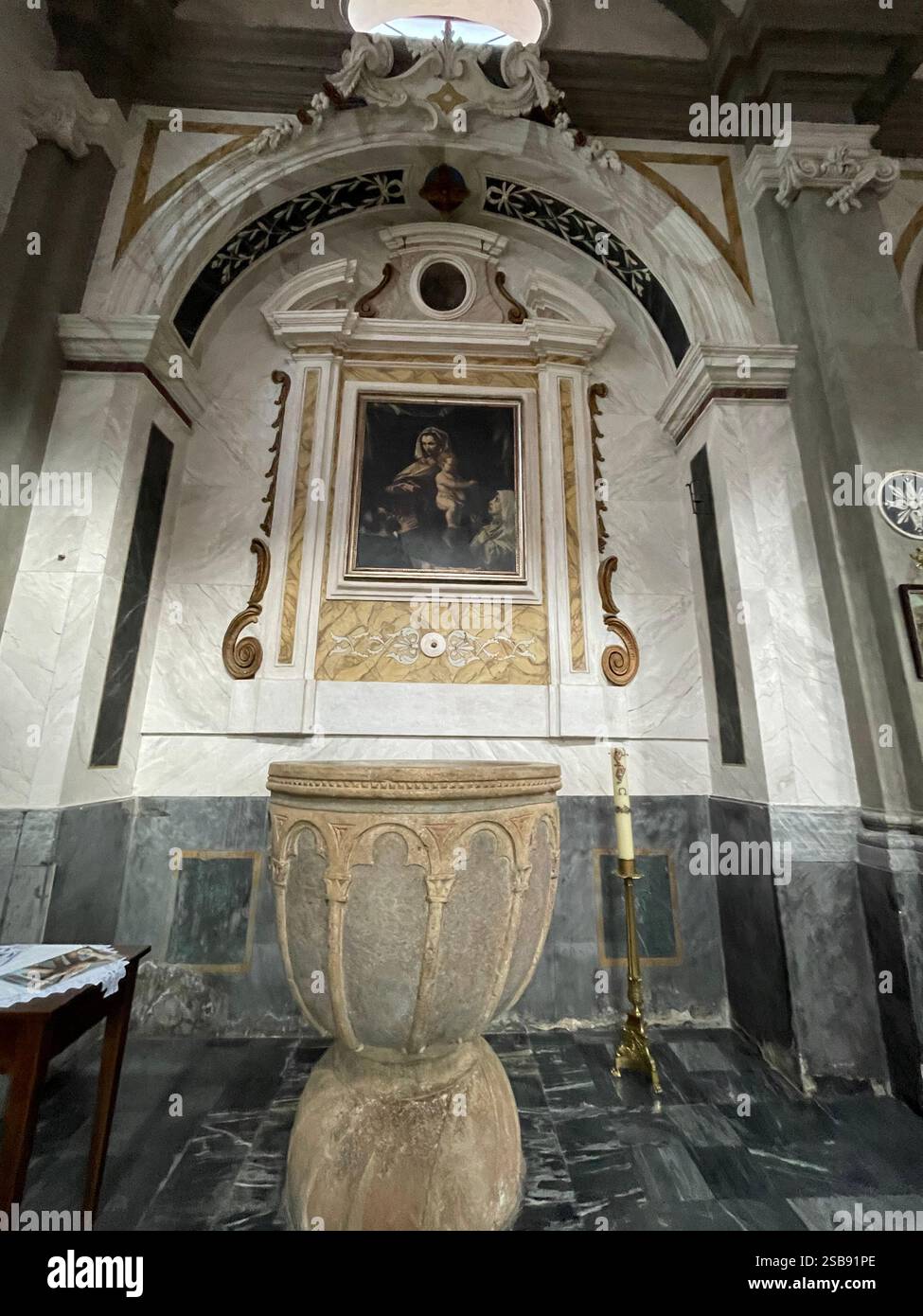Noci, Italy. Interior of the medieval Church of Saint Mary and Saint Roch (Chiesa madre). A baptismal font in front of a canvas of Madonna with child. - Smartphone Captured Stock Image