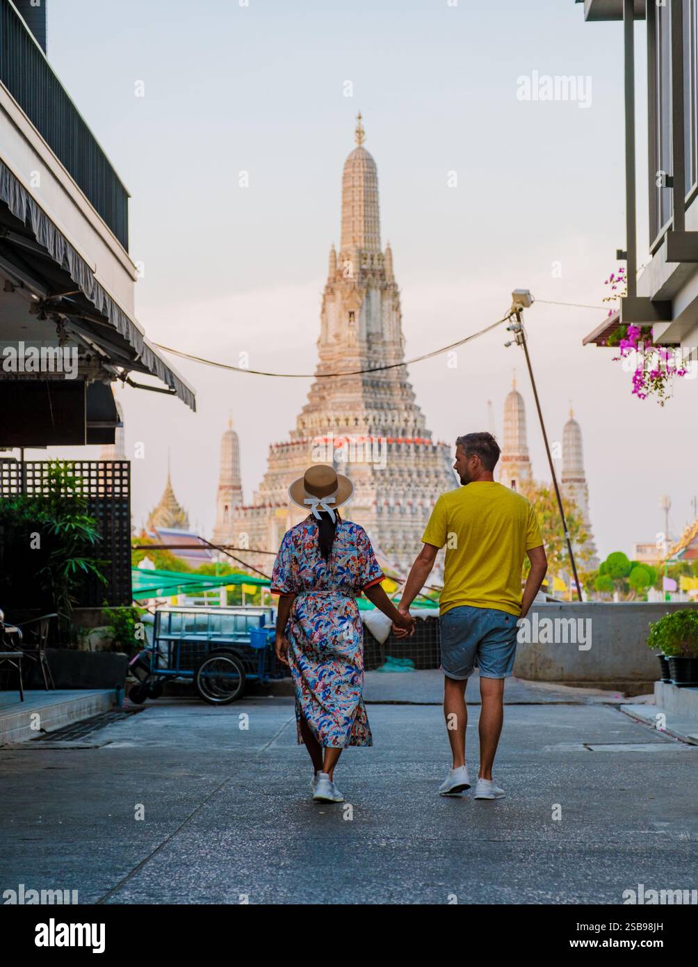 A couple walks hand in hand down a charming alley as the iconic Wat ...
