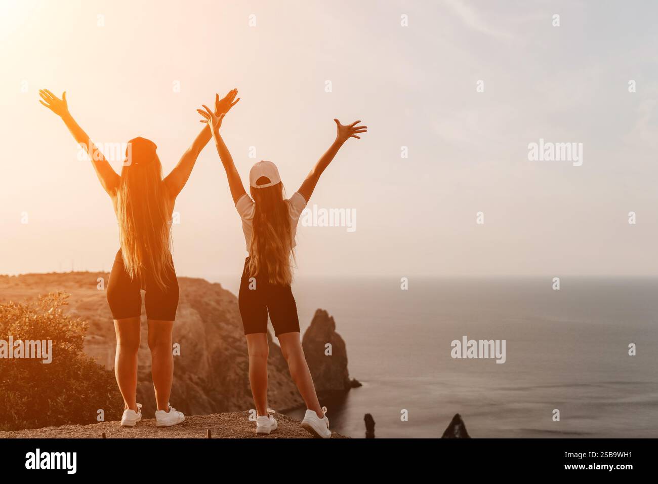 Two Girls Raising Their Arms in Victory on a Clifftop Stock Photo - Alamy