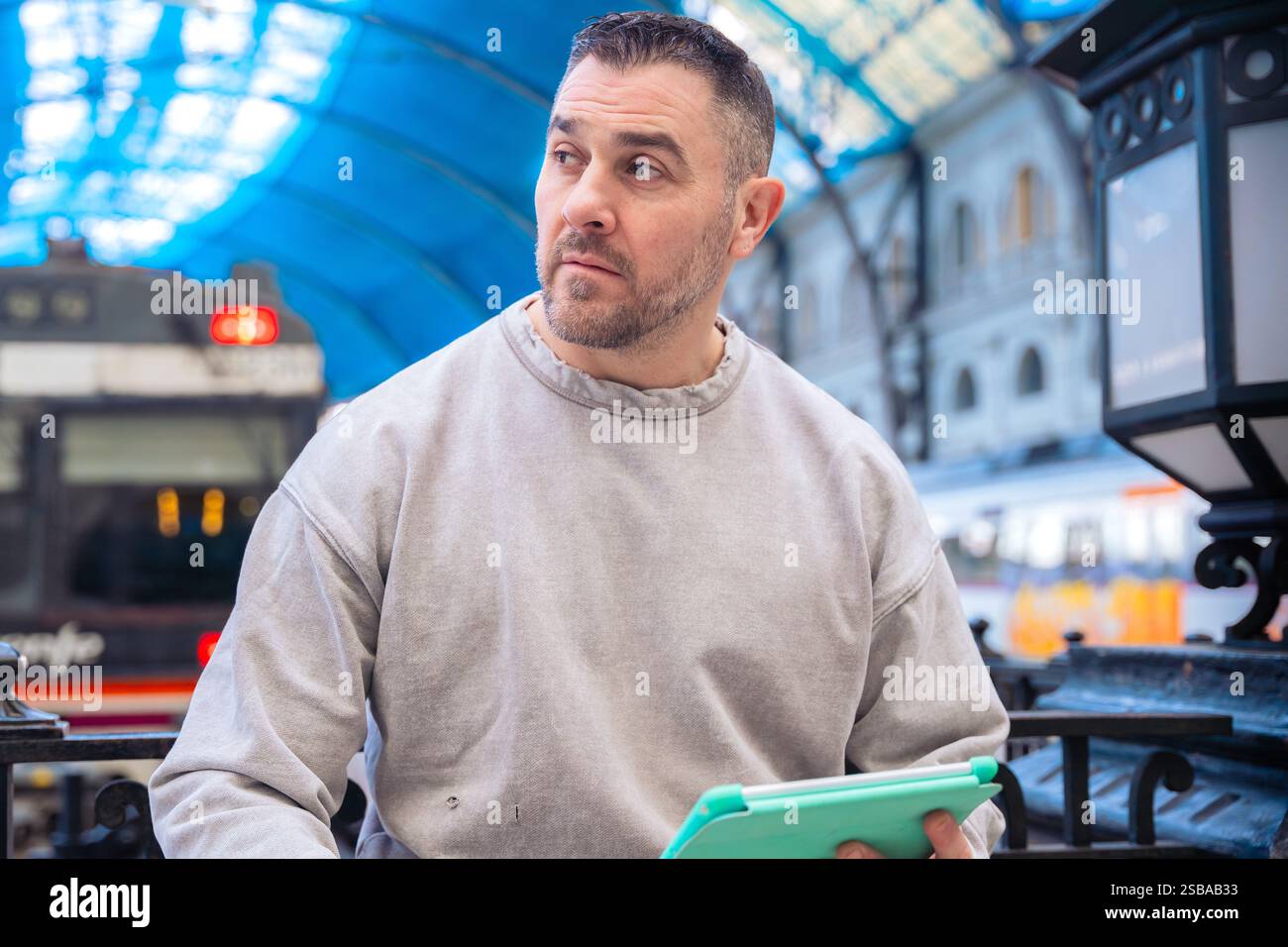 Focused Man Using Tablet While Waiting at Train Station looking at camera Stock Photo
