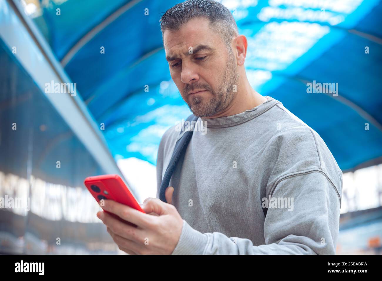 Man Using Red Smartphone at Train Station Stock Photo