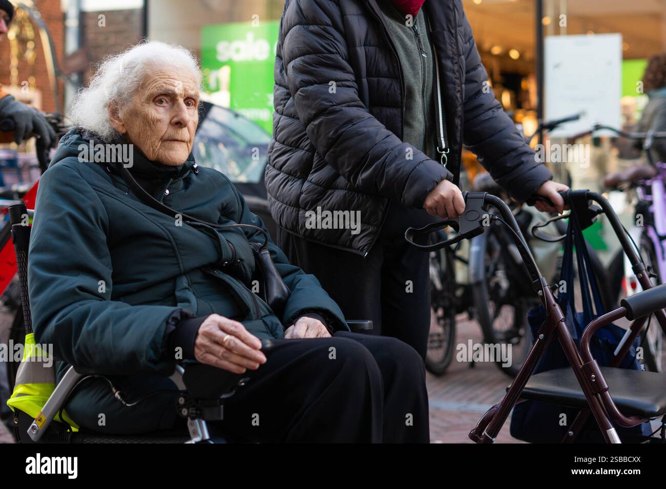 Mature woman walking with a walker next to elderly woman in wheelchair ...