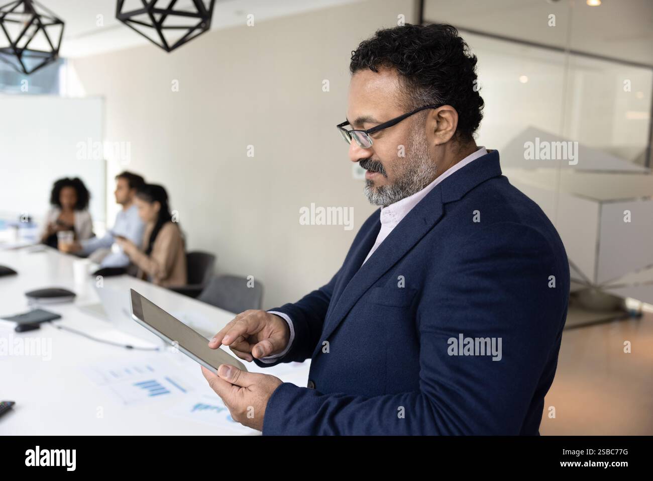 Focused mature Indian business leader man using digital tablet Stock Photo