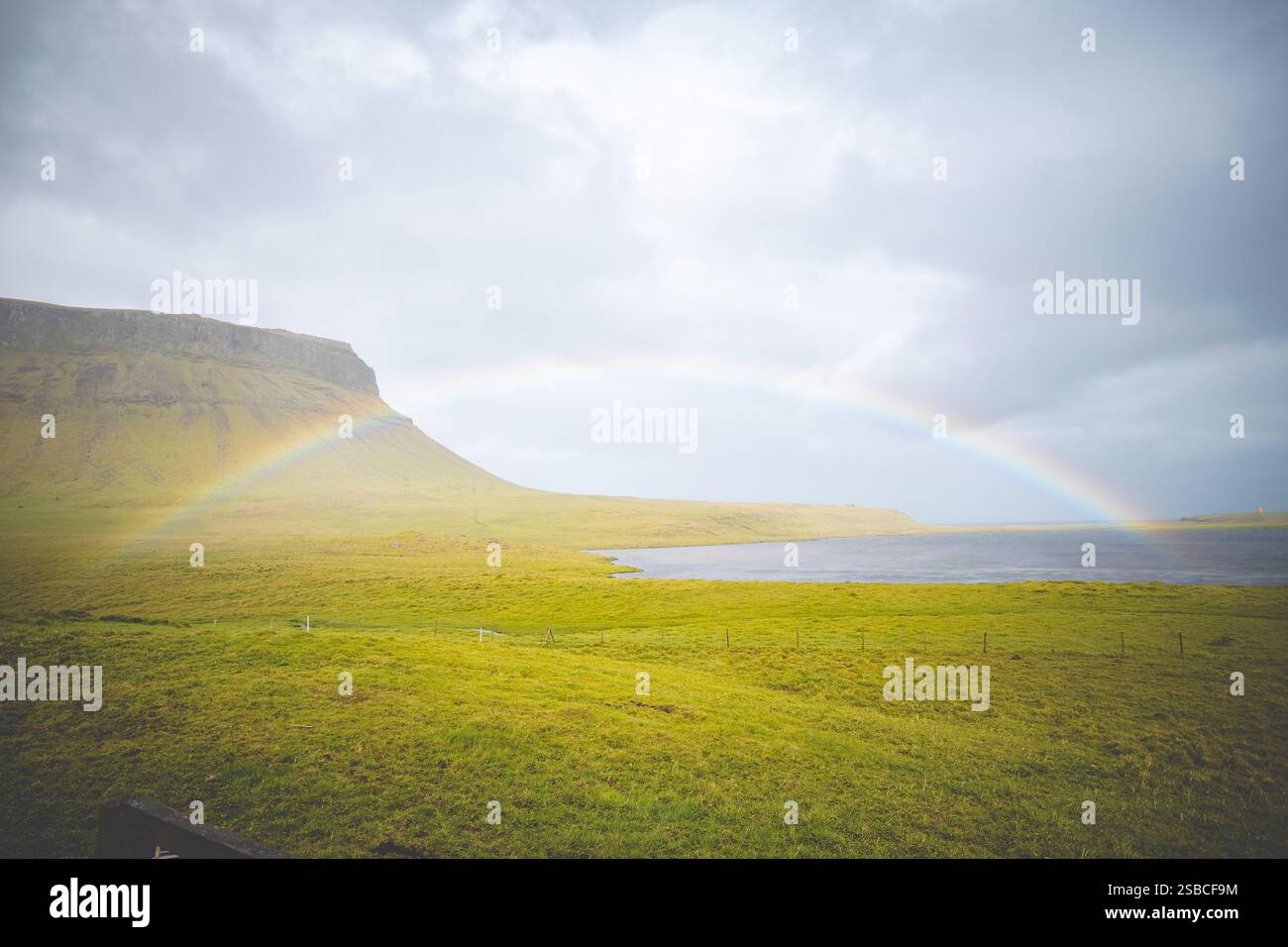 Vivid rainbow stretches across the cloudy sky above a serene Icelandic ...