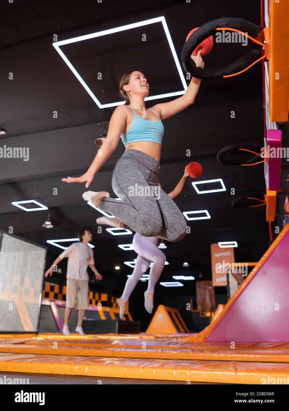 Young woman throwing ball in basket high jumping in trampoline arena ...