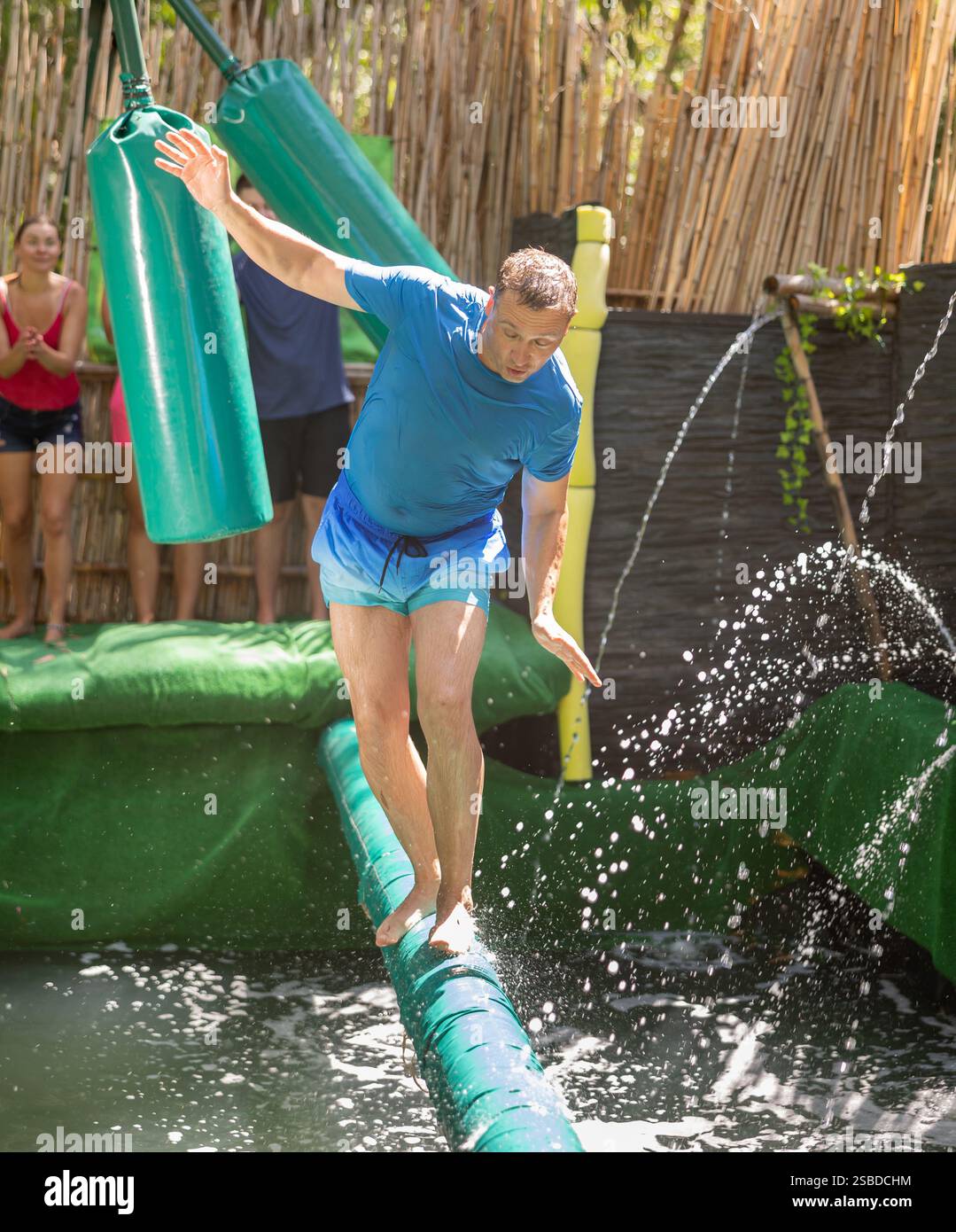 Swigging Pool Happy man passing on soft log between swinging bags over pool with ...