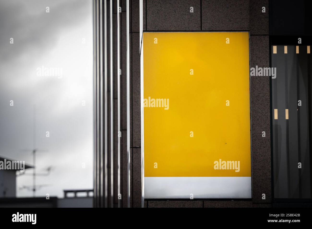 Selective blur on a A bright yellow sign hangs empty outside a modern storefront, awaiting custom branding. The bold, blank panel contrasts with the b Stock Photo