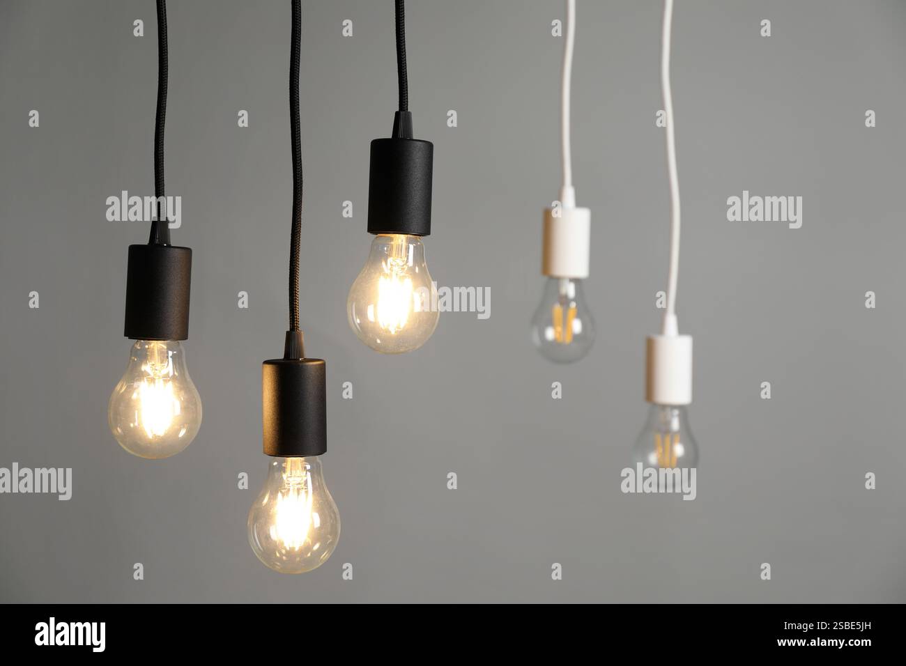 Light bulbs hanging on cords against grey background, selective focus Stock Photo