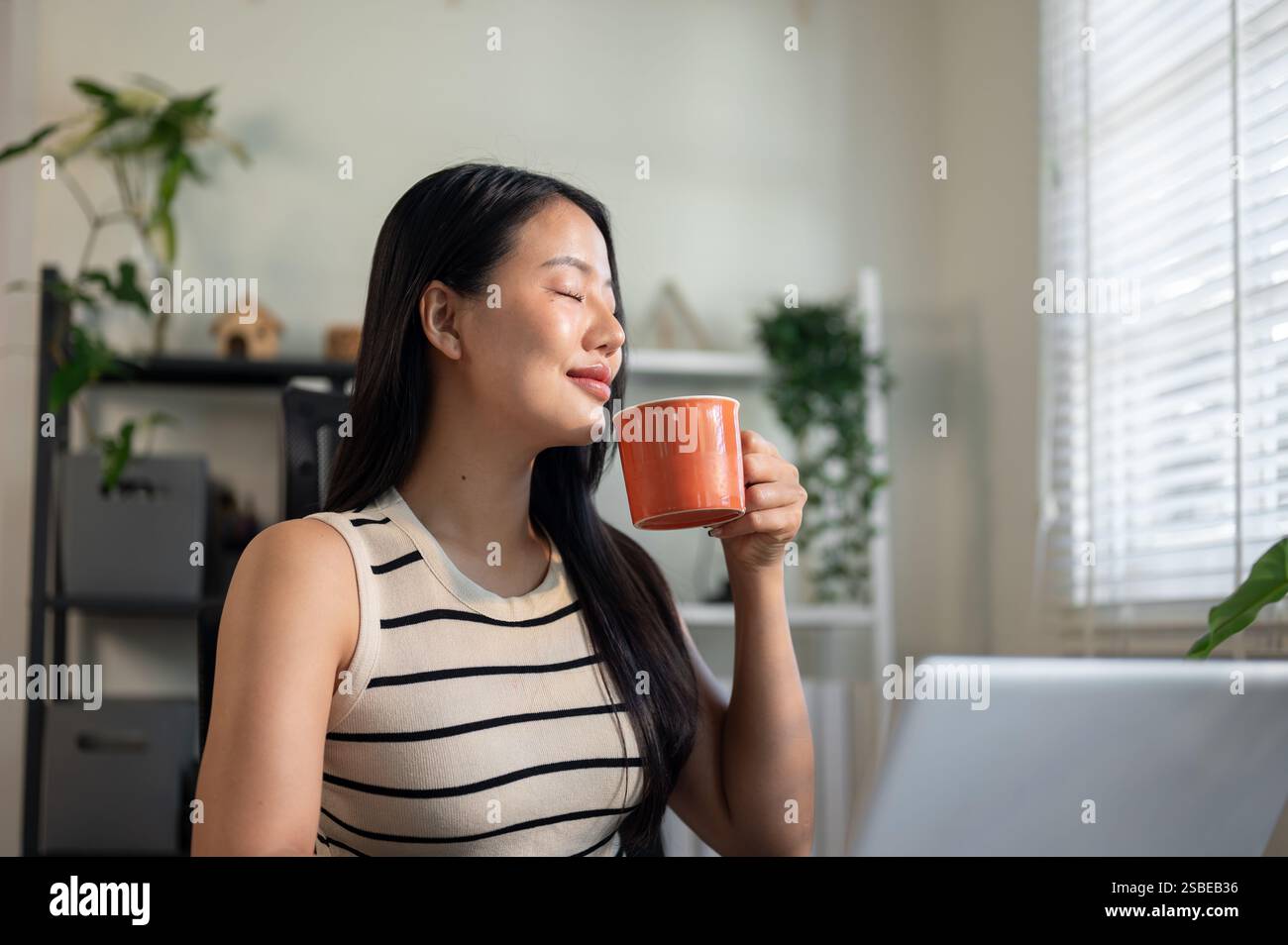 A relaxed, satisfied Asian businesswoman is enjoying her morning coffee ...
